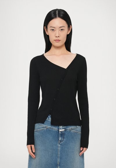 Schwarzer, gerippter Langarm-Cardigan mit V-Ausschnitt und asymmetrischem Knopfverschluss. Die Textur ist glatt und wird mit einem Jeansrock kombiniert.