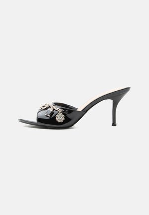 Mule à talon haut en cuir verni noir avec bout ouvert et breloques argentées décoratives comprenant une fleur et un cadenas sur la bride avant.