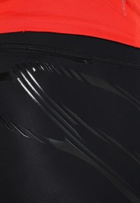 Leggings sportivi neri con una striscia nera lucida e una chiusura a zip in vita, abbinati a una maglietta rossa brillante.