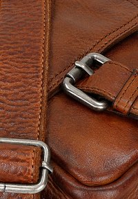 Bruine leren tas met een gestructureerde afwerking, voorzien van een zilveren metalen gesp en strapdetails. Gestikte randen en een gladde oppervlakte zichtbaar.