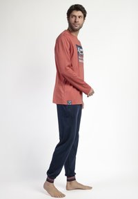 Camisa de manga larga color óxido con estampado gráfico, combinada con joggers azul marino con puños a rayas rojas y blancas. Material de mezcla de algodón.