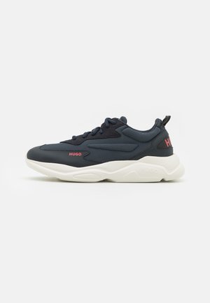 Ciemnoniebieski sportowy sneaker z czarnymi akcentami, białą masywną podeszwą, czerwonym logo "HUGO" po boku i na pięcie oraz czarnymi sznurówkami na białym tle.