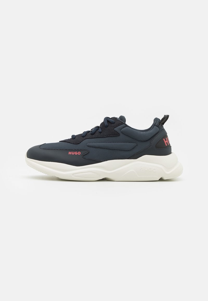 Baskets de sport bleu foncé avec des accents noirs, semelle blanche épaisse, logo rouge "HUGO" sur le côté et le talon, et lacets noirs sur fond blanc.