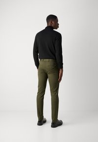 Zwarte lange mouwen top met een slim-fit ontwerp, gecombineerd met olijfgroene slim-fit broeken. De outfit wordt aangevuld met stijlvolle zwarte schoenen en een gladde textuur.