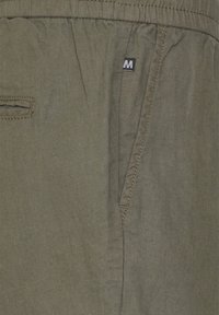 Olivově zelené bavlněné šortky s elastickým pasem, bočními kapsami a malou značkovou etiketou s bílým písmem na levé straně.