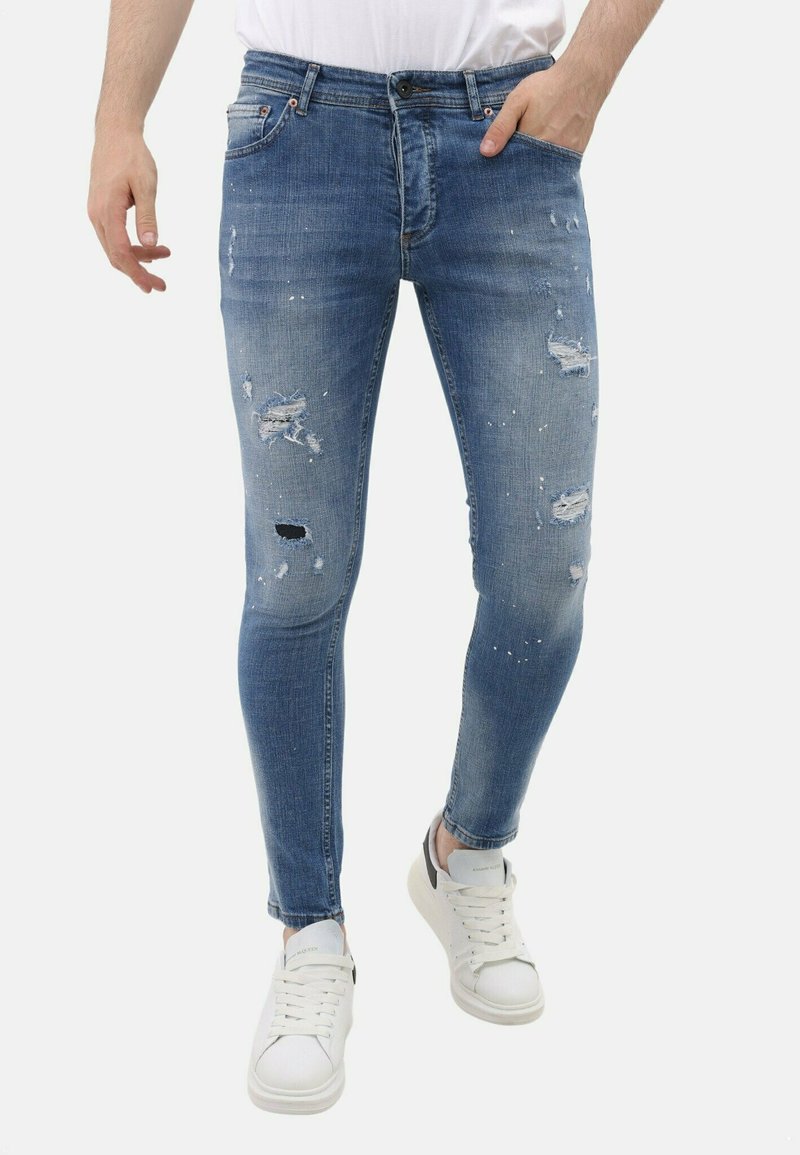 Lichtblauwe skinny jeans van denim met slijtage en scheuren. Heeft vijf zakken, een knoopsluiting en een licht vervaagde afwerking. Gecombineerd met witte sneakers.