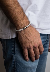 Nertas baltas apyrankė su lygiu metaliniu sagtimi, dėvima ant riešo, turinti tekstūruotą dizainą ir minimalistinę estetiką.