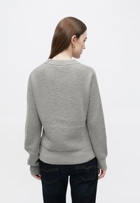 Hall hall, tekstuurse viimistlusega kudum, ümmarguse kaelusega ja pikkade varrukatega, kombineeritud tumedate teksapükstega.