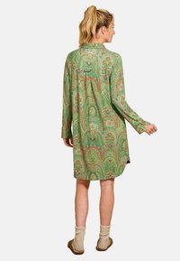 Long-sleeve green dress with intricate paisley pattern in various colors, featuring a buttoned back and relaxed silhouette.