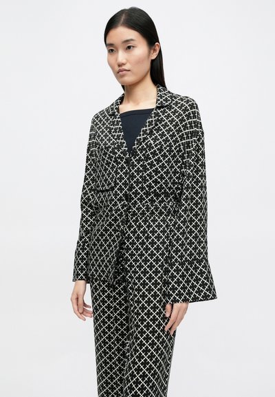 Μαύρο και λευκό ριγέ σύνολο που περιλαμβάνει πουκάμισο με γιακά, με κουμπιά και δύο μπροστινές τσέπες, συνδυασμένο με παντελόνι που ταιριάζει.