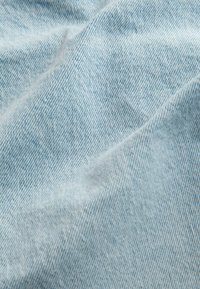Svetlomodrá denim látka s jemnou textúrou, viditeľným keprovým vzorom a drobnými vráskami, ktoré zdôrazňujú jej flexibilitu a neformálny vzhľad.
