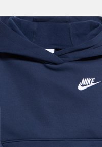 Marineblå hettegenser med brettet hette og hvit Nike-logo på brystet, laget av mykt stoff med synlige sømmer.