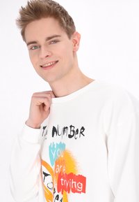 Vit sweatshirt med grafisk text och färgglada stänk i blått, orange och rött. Slät tyg, rund halsringning och avslappnad passform.