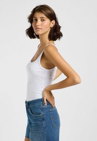 Weißes geripptes Tanktop mit dünnen Trägern, coupled mit blauen Jeansshorts. Das Outfit weist ein körperbetontes Design und einen klassischen Fünf-Taschen-Stil auf.