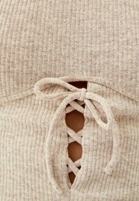 Beige gerippter Stricktop mit einem Schnür-Ausschnitt-Design und einer Schleifenverzierung. Der Stoff ist strukturiert und eng anliegend, betont die Taille.