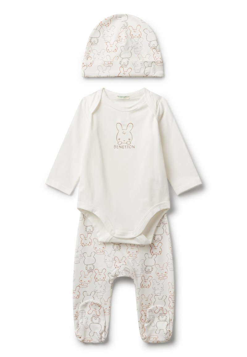 Bílý set oblečení pro miminko obsahující overal s dlouhým rukávem, který má na sobě obličej králíčka a text "Benetton", odpovídající kalhoty s králíčkovým potiskem a čepici.