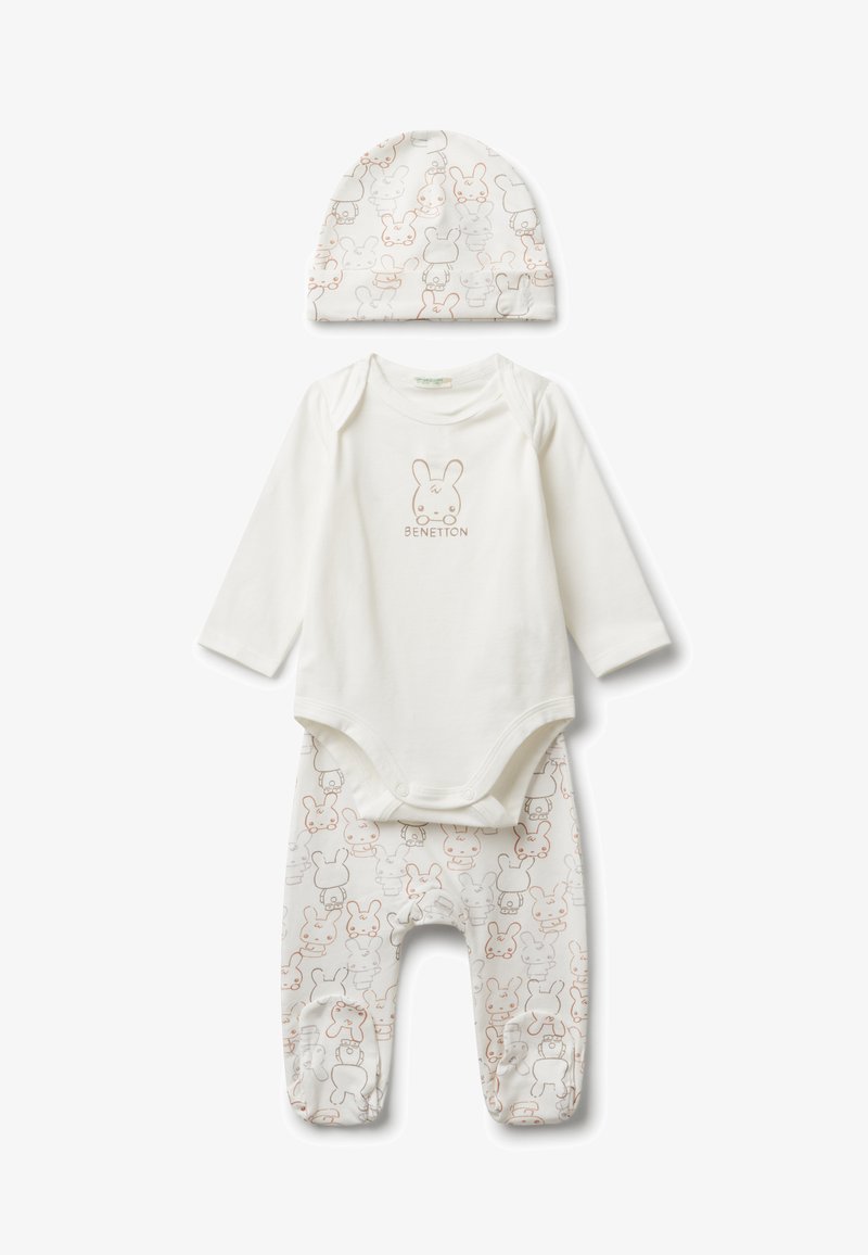 Bílý set oblečení pro miminko obsahující overal s dlouhým rukávem, který má na sobě obličej králíčka a text "Benetton", odpovídající kalhoty s králíčkovým potiskem a čepici.