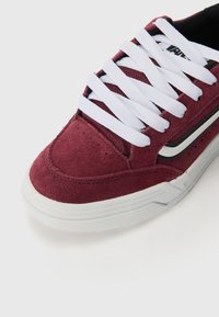 Maroon suede sneaker with white laces, black accents, and textured rubber sole. Features a round toe and stitched detailing.