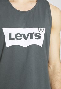 Mörkgrå ärmlös tröja i bomull med en vit Levi's-logotyp i fet svart teckensnitt över bröstet. Slät tygkänsla.