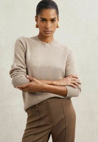 Pulover bej tricotat cu guler rotund și manșete cu nervuri, asortat cu pantaloni brown personalizați. Textură moale și croi lejer.