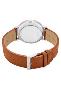 Montre Skagen avec un boîtier en métal argenté et un bracelet en cuir marron. Le bracelet présente une finition texturée et une boucle en argent.