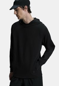 Mustat pitkähihainen huppari, joka on valmistettu pehmeästä kankaasta. Hupparissa on kengurutasku, raglan-hihat ja vähäistä brändäystä helmassa.