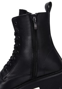 Bottine en cuir noir avec une fermeture éclair sur le côté, bout rond et lacets à l'avant avec œillets métalliques et semelle texturée.