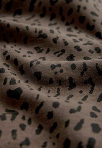 Brunt tyg med en mjuk textur, som har ett svart leopardmönster med fläckar i olika storlekar spridda över ytan.