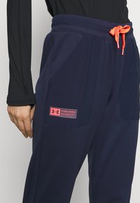 Marineblaue Sporthose mit elastischem Bund und verstellbarem roten Kordelzug, ausgestattet mit Seitentaschen und einem leuchtend roten Markenschild.