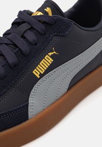 Navy and gray sneaker made of leather and suede, featuring a rubber sole, golden logo, and contrasting stitching details.