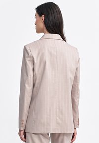 Jasnoróżowy żakiet w paski o dopasowanym kroju, z wyłamywanym kołnierzem i mankietami na trzy guziki. Gładka tekstura i pionowe prążki podkreślają design.