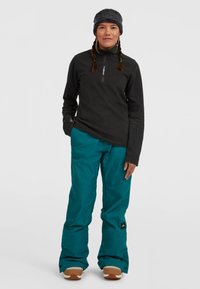 Svart fleece tröja med kvartslång dragkedja och teal snöbyxor, med en avslappnad passform, strukturerad tyg och tan-färgade detaljer på snöskor.