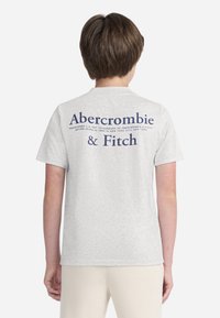 Maglietta in cotone grigia a maniche corte, con testo blu sul retro che recita "Abercrombie & Fitch" e una nota di marchio registrato sotto.