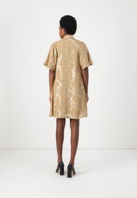 Vestito corto a maniche corte, lungo fino al ginocchio, in un leggero beige con un motivo a catena argentata. Presenta una vestibilità comoda e un colletto tondo. Scarpe nere con tacco alto.