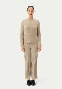 Beige ribbstickad tröja med långa ärmar, tillsammans med matchande ribbstickade byxor. Outfiten har en figurnära siluett med en subtil textur.