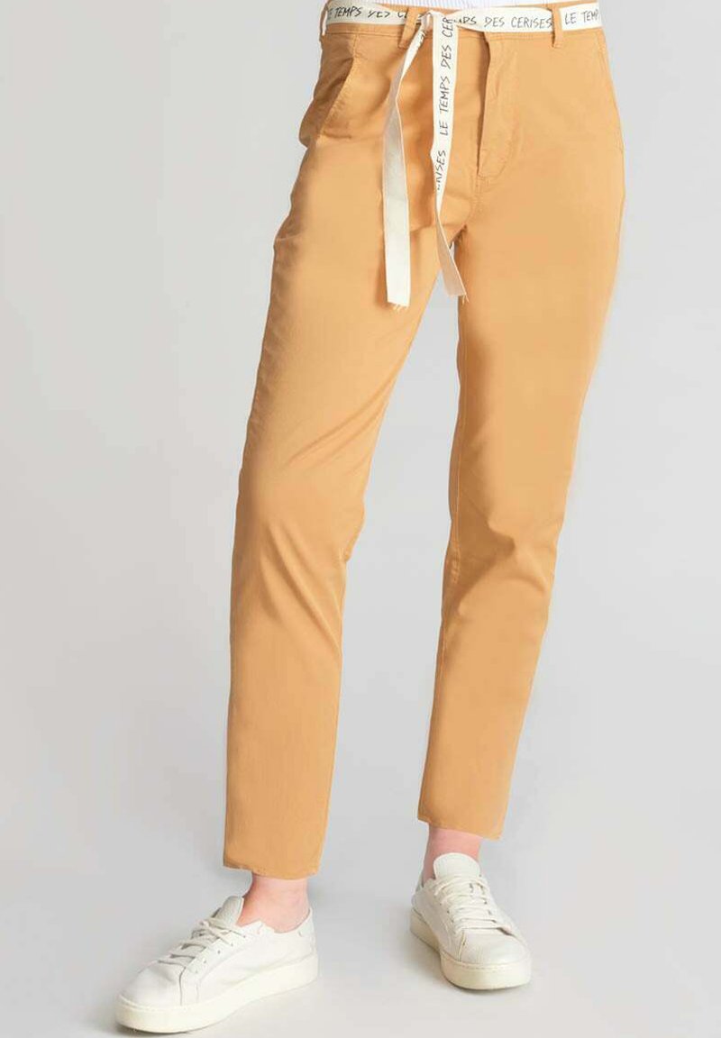 Pantaloni di cotone color senape a gamba slim, dotati di tasche laterali e una vita con cordoncino bianco a contrasto. Indossati con sneakers bianche.