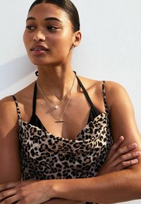 Haut en imprimé léopard avec un décolleté drapé, des bretelles noires et des colliers en or superposés avec un pendentif en perle et en barre. Texture lisse.