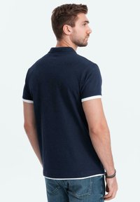Marineblauw polo-shirt van katoen met witte accenten op de mouwen, korte mouwen en een klassieke kraag. Draagt bij denim jeans.