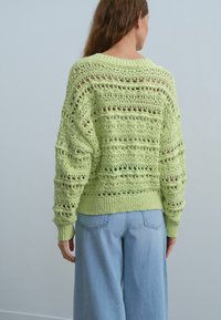 Pull en crochet vert clair avec un tissage ouvert, manches longues et poignets côtelés. Associé à un jean en denim clair à jambes larges.