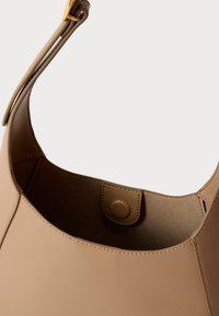 Pruun nahast õlakott, sileda tekstuuriga, ümar top, klõpskinnitusega ja lame rihm kandmiseks. Sisemine vooder on beež.