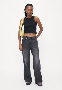 Top cropped preto combinado com jeans cinza de perna larga e cintura alta. Os acessórios incluem uma pequena bolsa verde limão brilhante e sapatos roxos.
