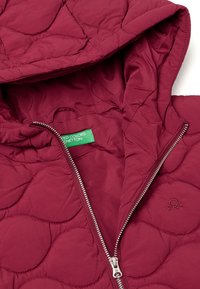 Prošívaná vínová bunda s kapucí, stříbrným zipem a zelenou nášivkou uvnitř. Texturovaný povrch sobloukovými vzory a vyšívaným logem.