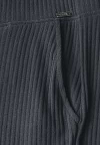 Donkergrijze geribbelde tricot stof met een opvallende textuur, voorzien van een subtiele logo-tag met de tekst "CECIL" in de tailleband.