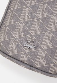 Gray textured material featuring a geometric pattern with cream accents. Includes a small, embossed crocodile logo and logo text.