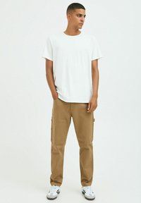 White cotton t-shirt paired with brown cargo pants featuring side pockets, worn with white sneakers. Simple and casual design.