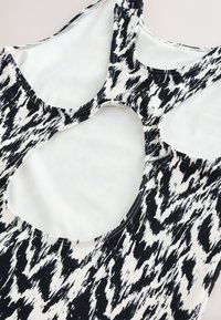 Top sans manches à motif abstrait noir et blanc avec un grand détail découpé arrondi dans le dos, posé à plat sur une surface claire.