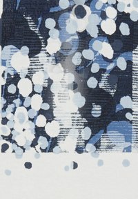 Textiel met een textuur, gekenmerkt door een blauw-witte cirkelprint met variërende dotgroottes, die contrasteert met een overwegend donkere achtergrond.