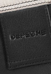 Crni kožni zakrpa s utisnutim logom "DEPECHE", prošivenim rubovima i teksturiranom površinom. Pozadina je od svijetlog sintetičkog materijala.