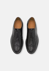 Zapatos de vestir de cuero negro con un acabado pulido, diseño de punta alada, detalles perforados y cierre de cordones. Plantilla color marrón visible.