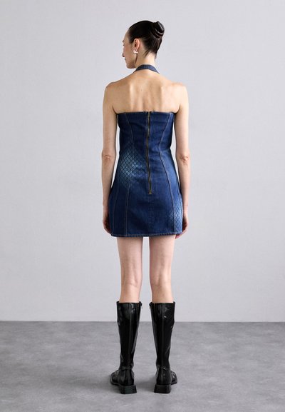 Denim halter mini haljina s pripijenim korzetom, stražnjim zatvaračem i teksturiranim uzorkom na dnu. Uparena s crnim čizmama do koljena.